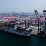 Alt Text: "A cargo ship at a U.S. port with towering cranes, highlighting the need to fix cybersecurity maritime issues in critical systems."