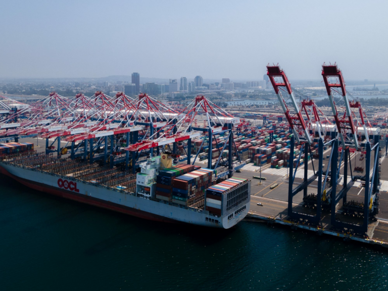 Alt Text: "A cargo ship at a U.S. port with towering cranes, highlighting the need to fix cybersecurity maritime issues in critical systems."